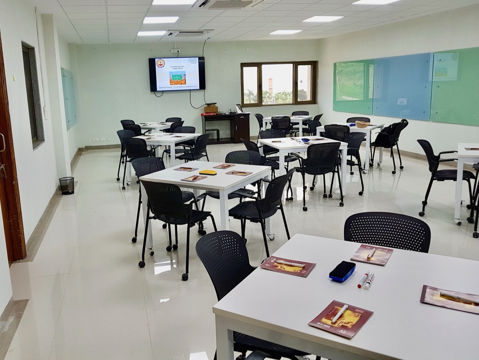 CREATES Learning Lab: movable square tables and castored chairs, colored glass writing boards, and a wall display, set up for a faculty workshop.